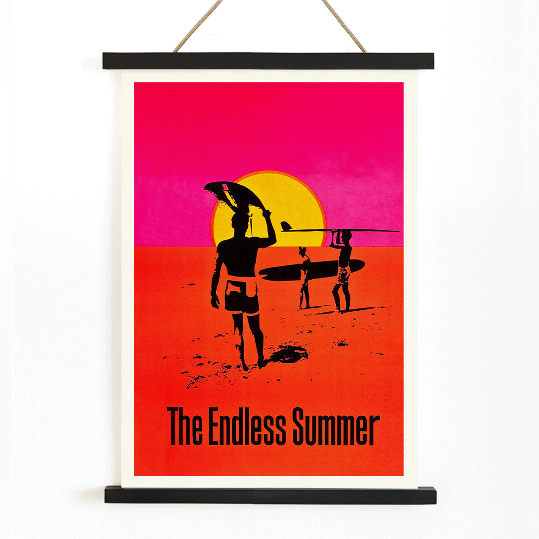 The Endless Summer poster with surfers carrying boards on a beach at sunset against a stylized sunset backdrop, with wooden magnetic frame on white background