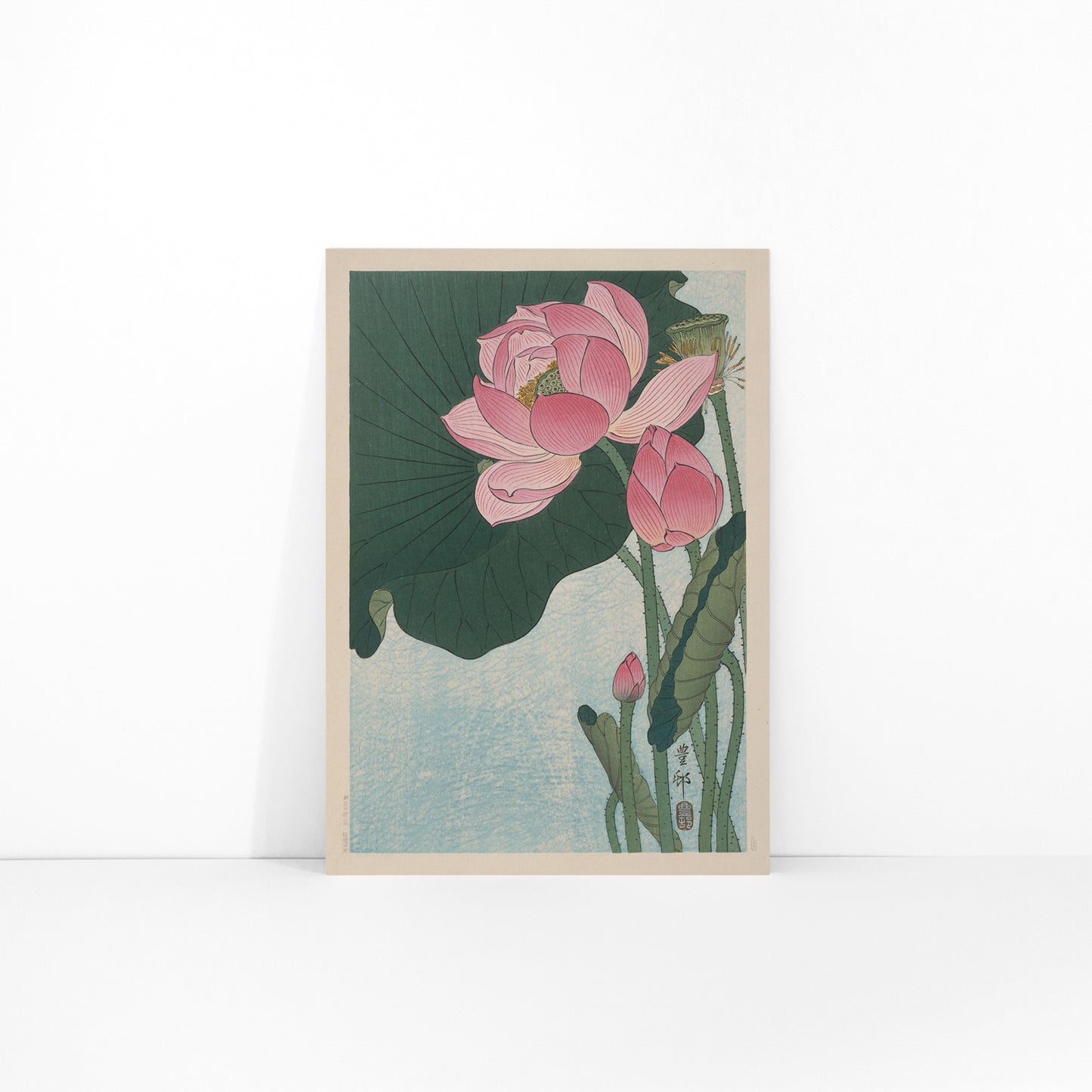 Pink lotus flowers and green leaves in Japanese woodblock print poster by Ohara Koson with light blue background, framed and displayed in modern living room decor