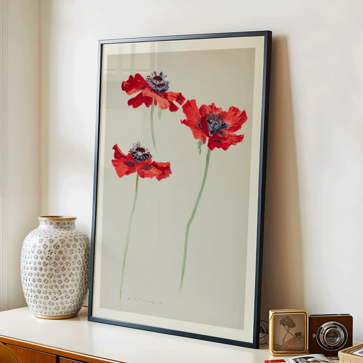 Three Studies of Poppies by Sophia Crownfield poster featuring vibrant red poppies on delicate stems and a light background artwork, framed and displayed in modern living room decor