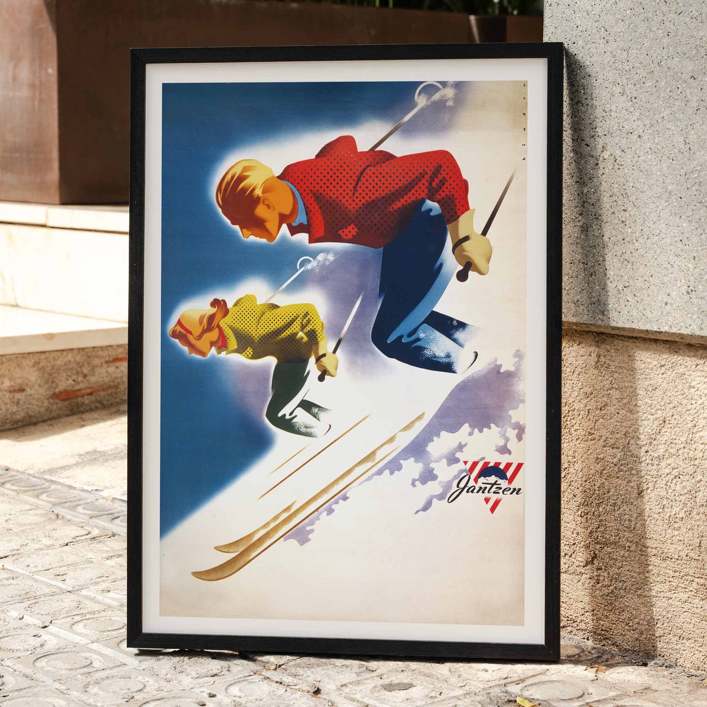 Vintage skiing poster of man and woman skiing downhill in bold colors by Joseph Binder for Jantzen, framed and displayed in home decor