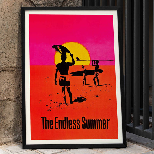 The Endless Summer poster with surfers carrying boards on a beach at sunset against a stylized sunset backdrop, framed and displayed in home decor