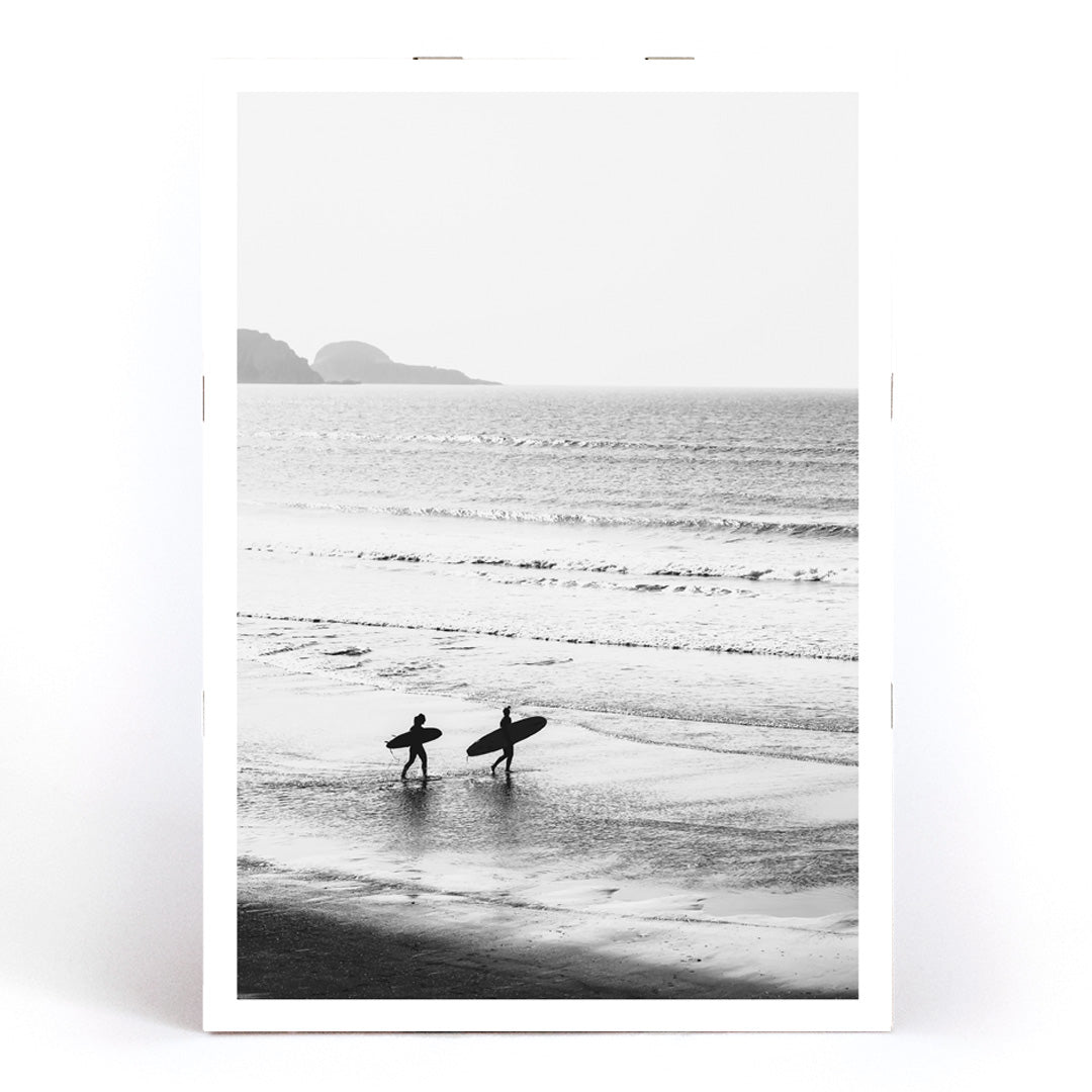 Black and white poster of surfers walking along the beach Surfers walking on the beach artwork, framed and displayed in modern living room decor